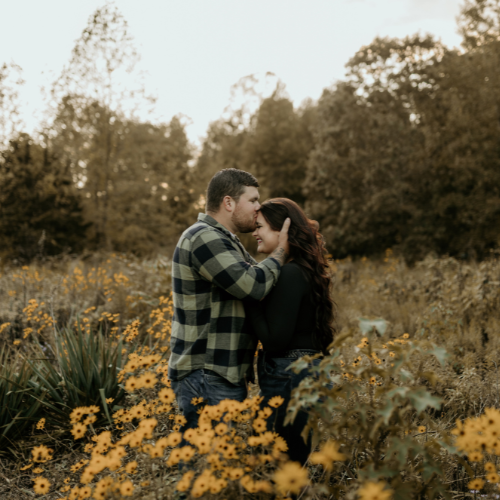 Couple in flower field -- male partner is holding girls hair, leaning in to kiss forehead