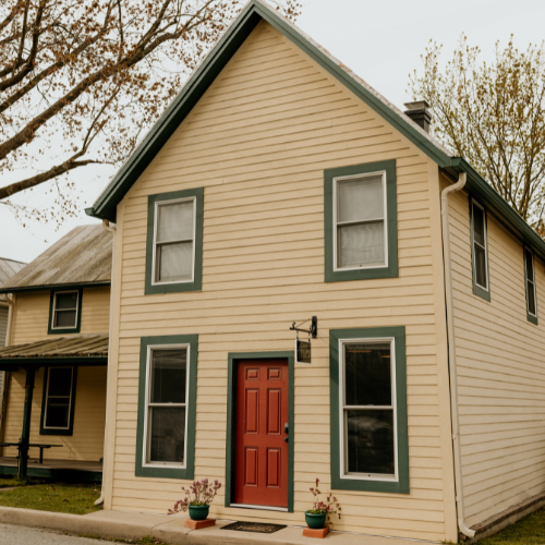 Image of a historic home, with yellow Siding with a Red Door